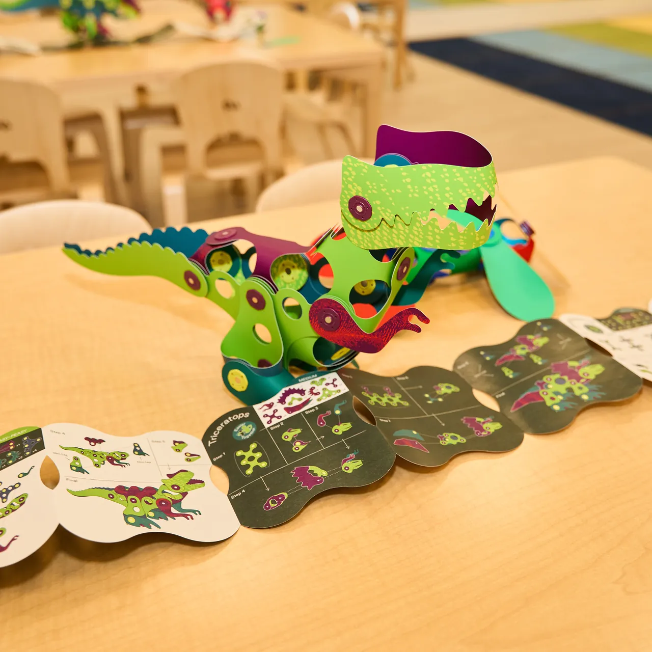 A Clixo dinosaur on a classroom table next to an activity booklet