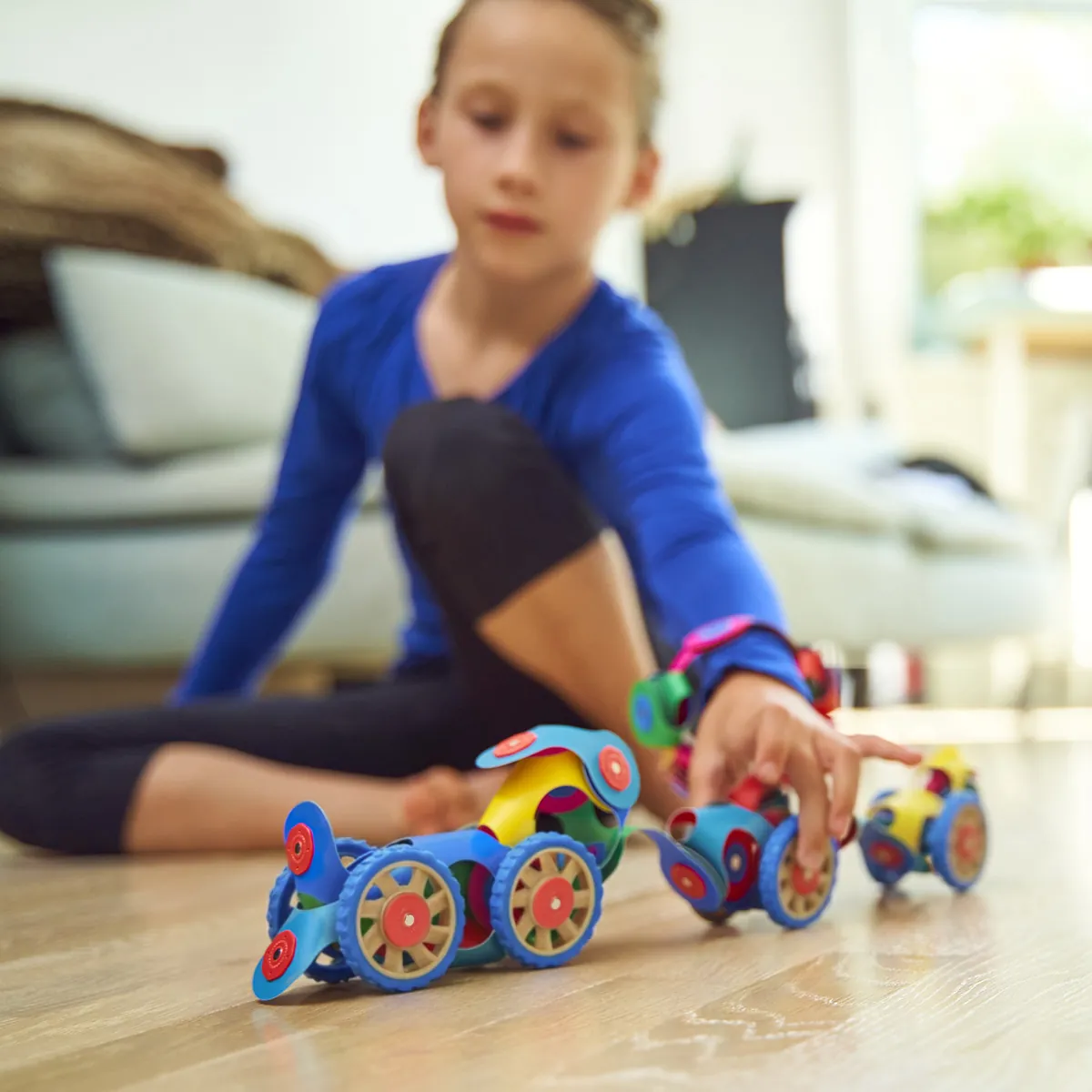 A girl on the floor rolling a row of Clixo vehicles with wheels